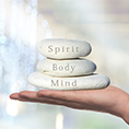 Drei weisse Steine auf einer Hand mit der Aufschrift: Spirit, Body, Mind